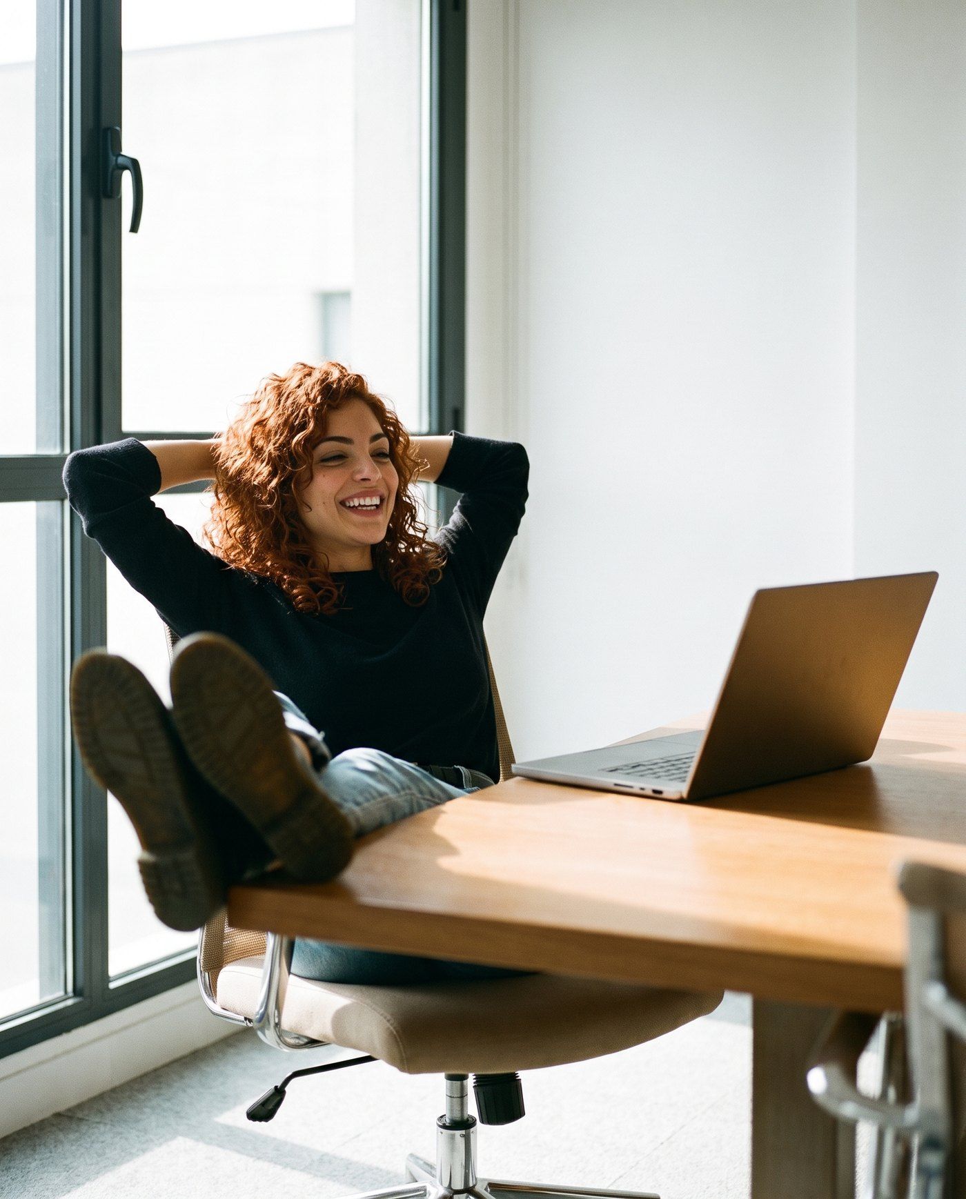 Lisa lehnt sich im Büro zurück, die Füße auf dem Tisch, und lacht. Vor ihr steht der Laptop.